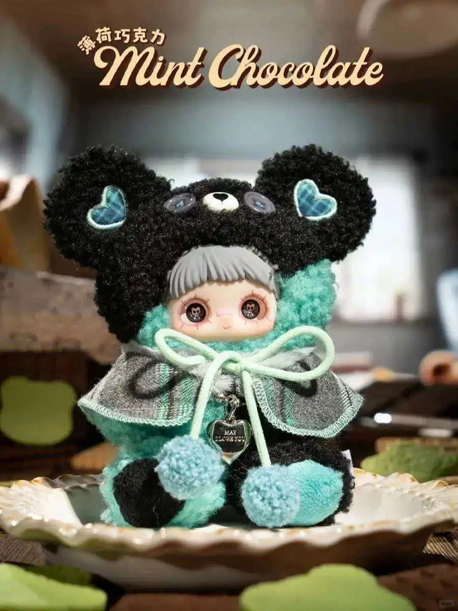 A cute black and teal plush charm of a bear with large eyes sitting on a white plate.
