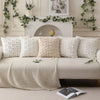 A collection of cream and white textured pillow covers with embroidered daisy designs displayed on a sofa.