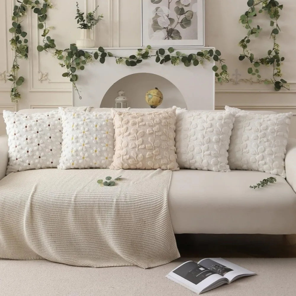 A collection of cream and white textured pillow covers with embroidered daisy designs displayed on a sofa.