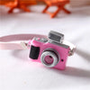 Accessoire de caméra rose avec objectif monté sur une sangle blanche, sur fond blanc.