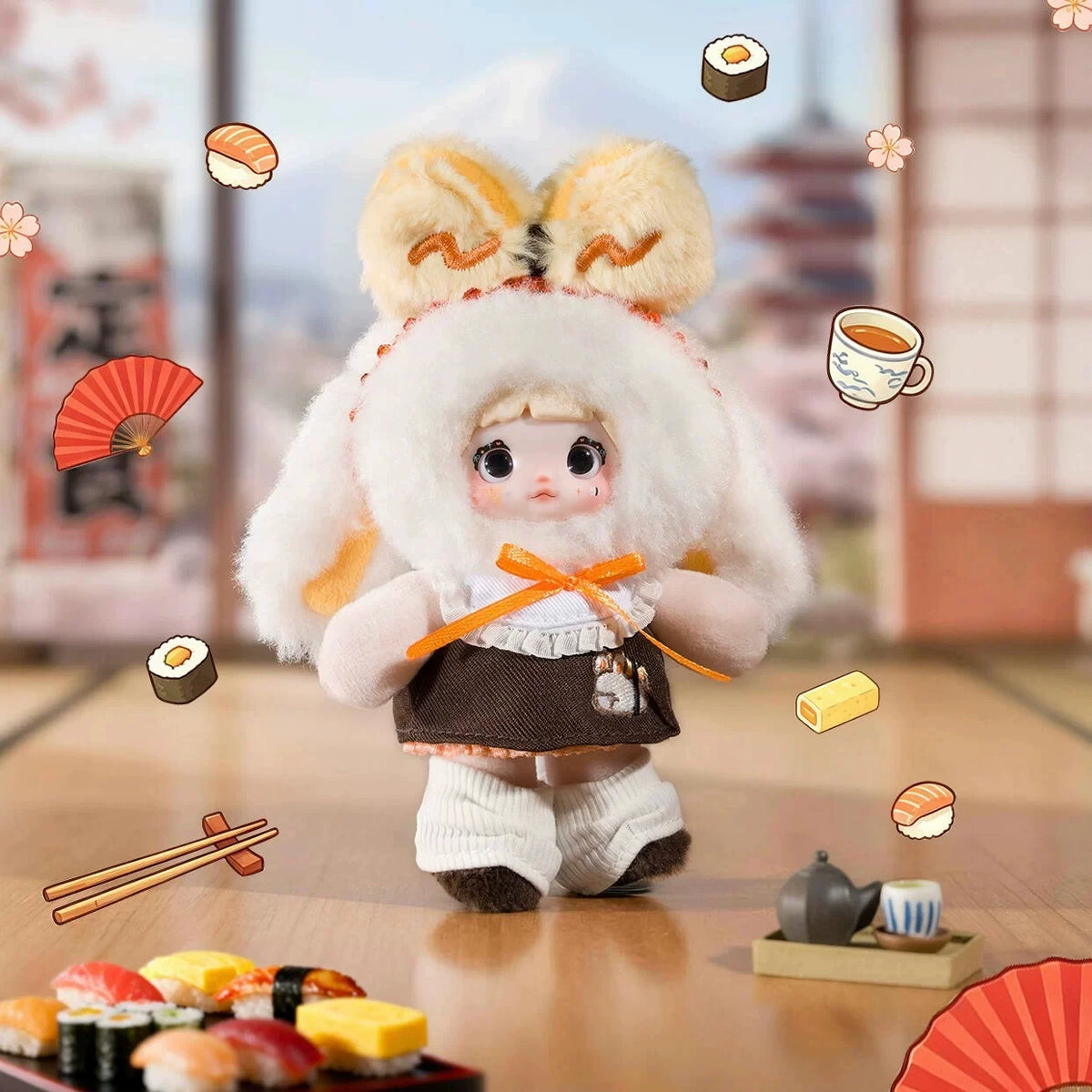 A fluffy white plush keychain of a character dressed in traditional Japanese attire, surrounded by various food items.