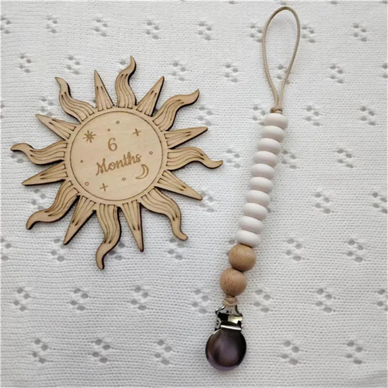 A wooden sun-shaped pacifier clip with a silicone teether and a leather cord.