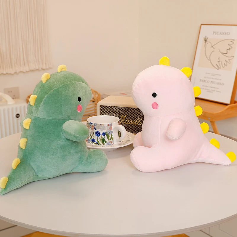 A green dinosaur plush toy and a pink unicorn plush toy are displayed on a white table.