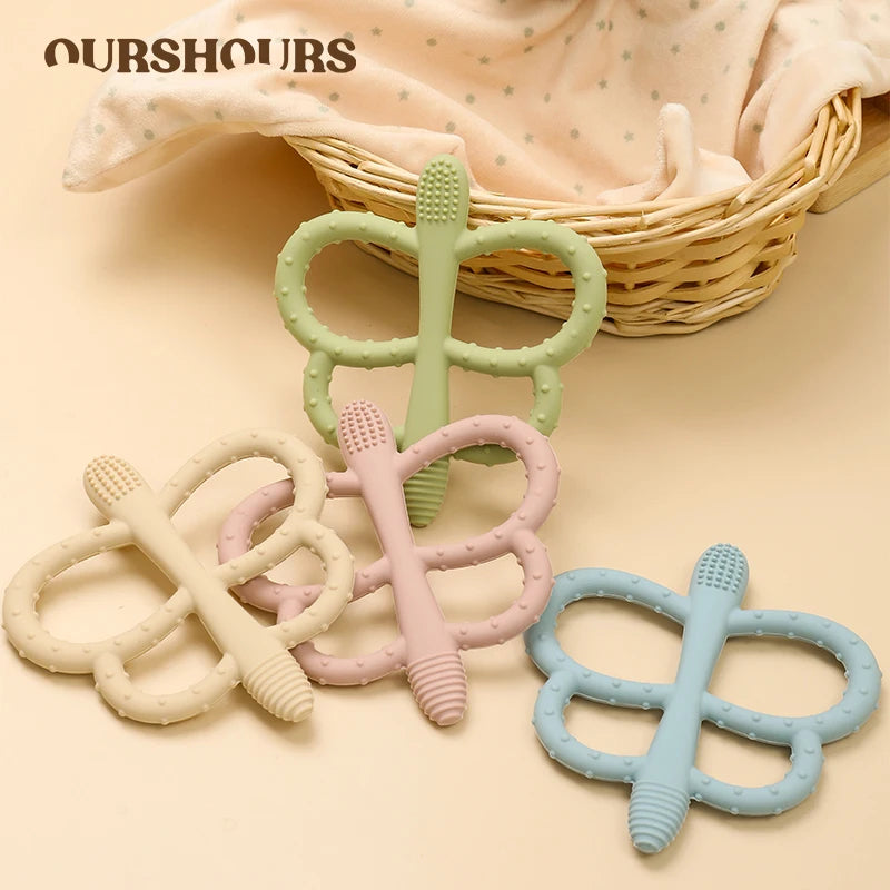A collection of soft silicone butterfly teethers in green, pink, and blue are displayed next to a woven basket.