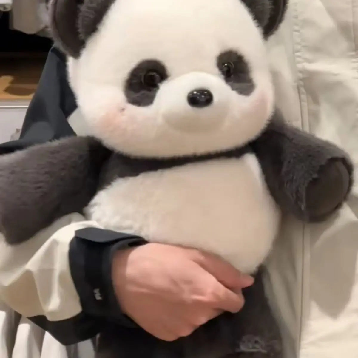 A close-up of a cute running panda stuffed animal with black and white fur being held by a person.