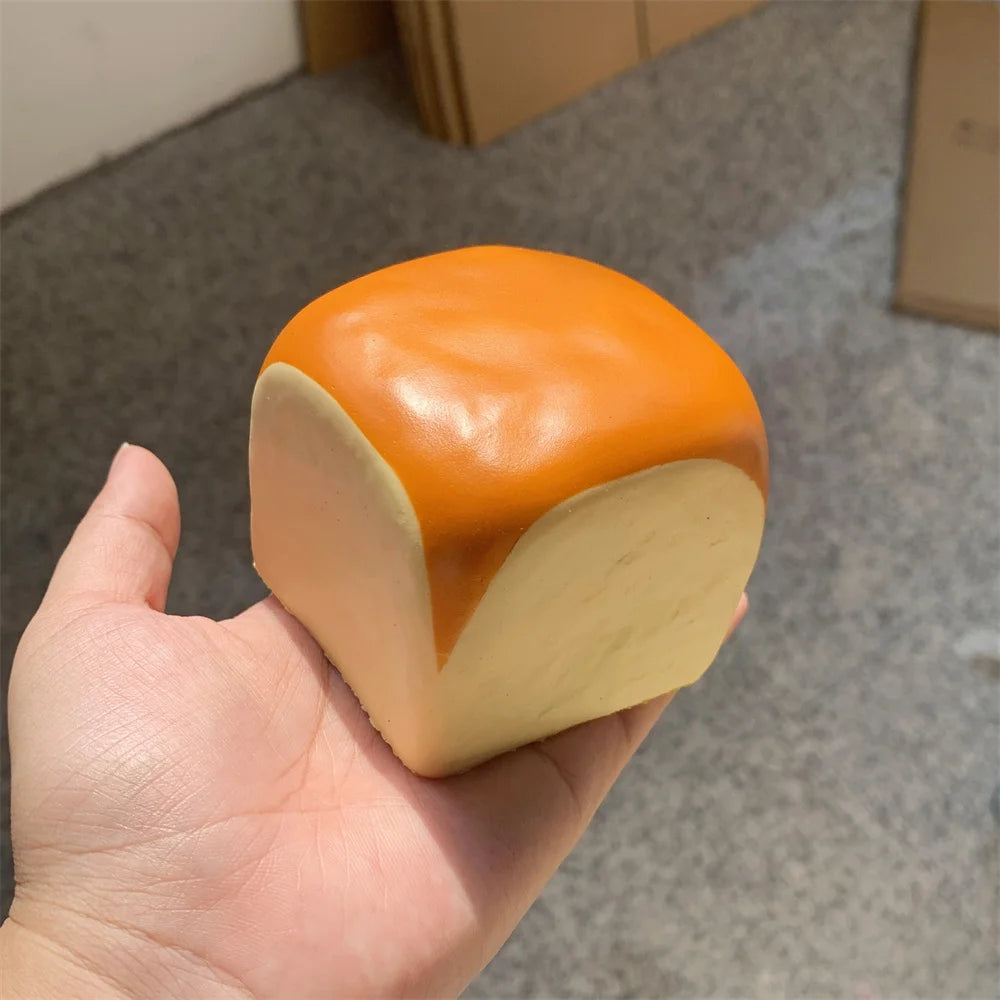 Une main tient un jouet de petit pain décoratif avec un dessus orange et un corps de couleur crème.