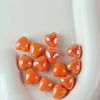 A pile of small, glossy orange heart-shaped ceramic beads for jewelry making.