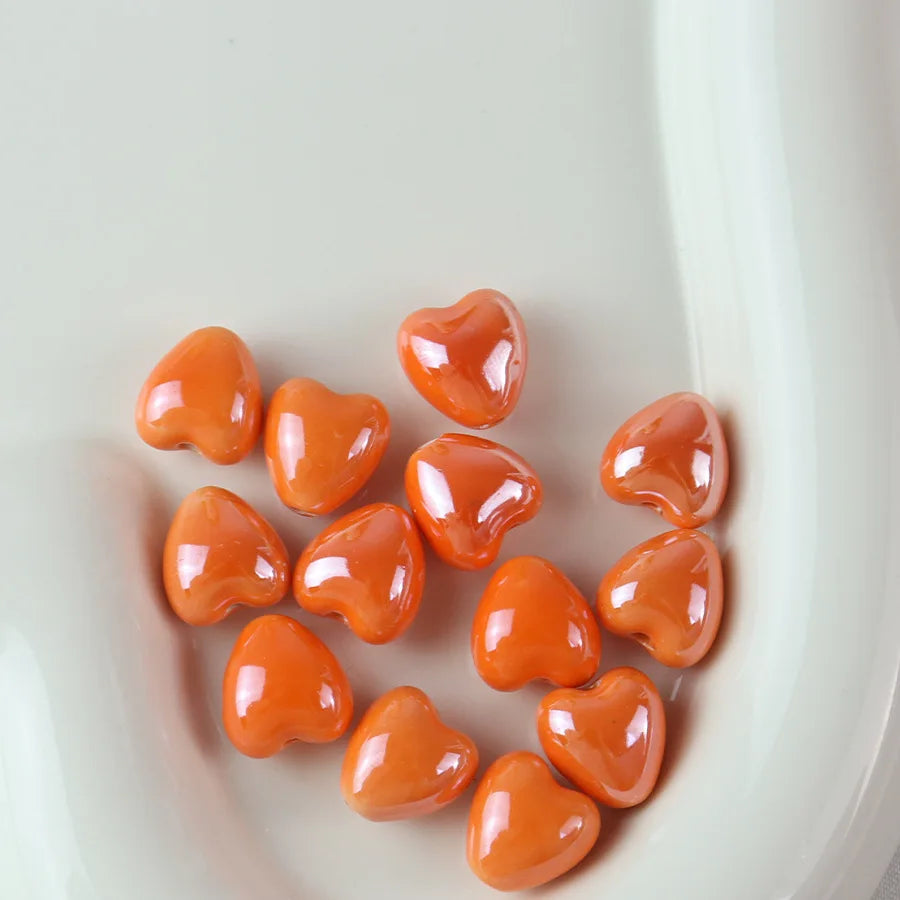 A pile of small, glossy orange heart-shaped ceramic beads for jewelry making.