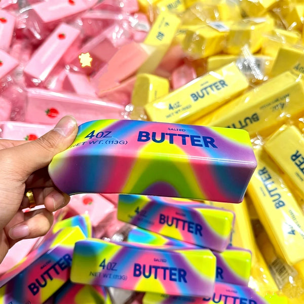 A hand holds a purple and pink butter stick fidget toy in a pile of yellow squishy stress relief products.