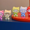 A row of colorful cat-shaped mini figurines in various pastel colors displayed on a red surface.