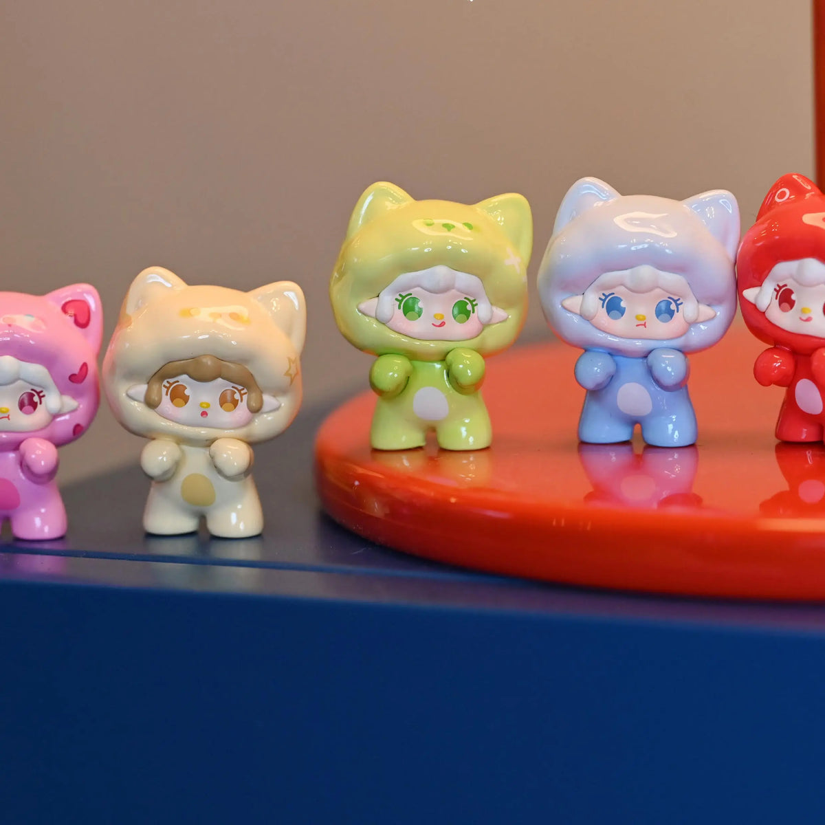 A row of colorful cat-shaped mini figurines in various pastel colors displayed on a red surface.