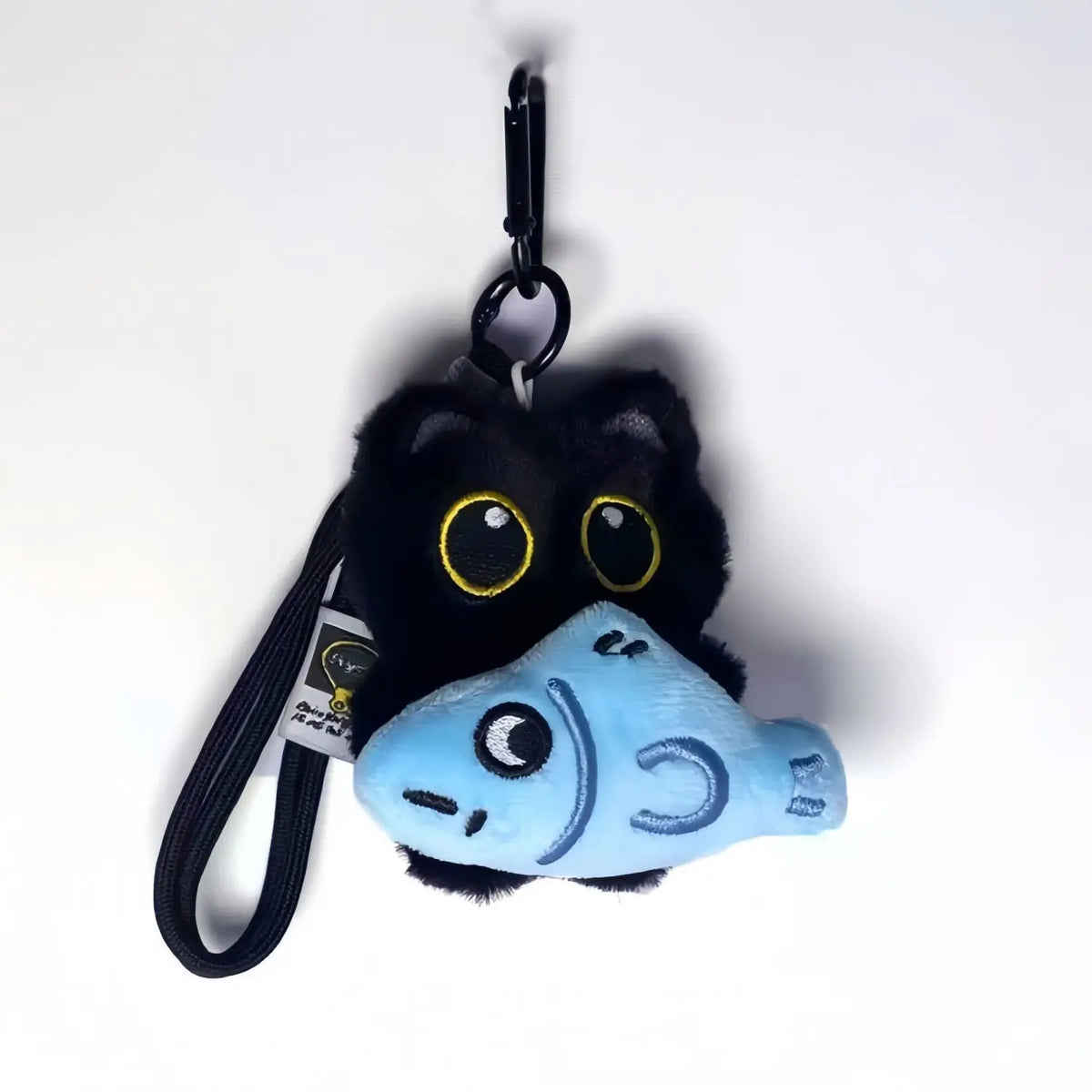A cute plush black cat charm with large yellow eyes and a light blue fish head, attached to a black keychain.