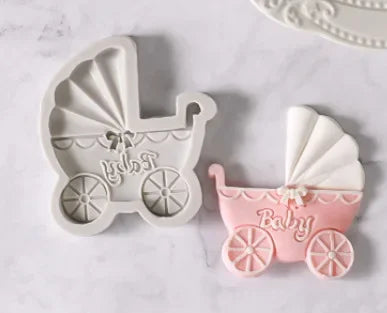 A set of white silicone baby-themed cake molds including a stroller, bottle, and pacifier in pink and white.