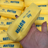 A hand holds a yellow butter stick squishy stress ball with the text 40z butter salted visible on the packaging.