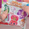 A hand holds a package of Calico Critters figures, including a pink and purple animal figure.