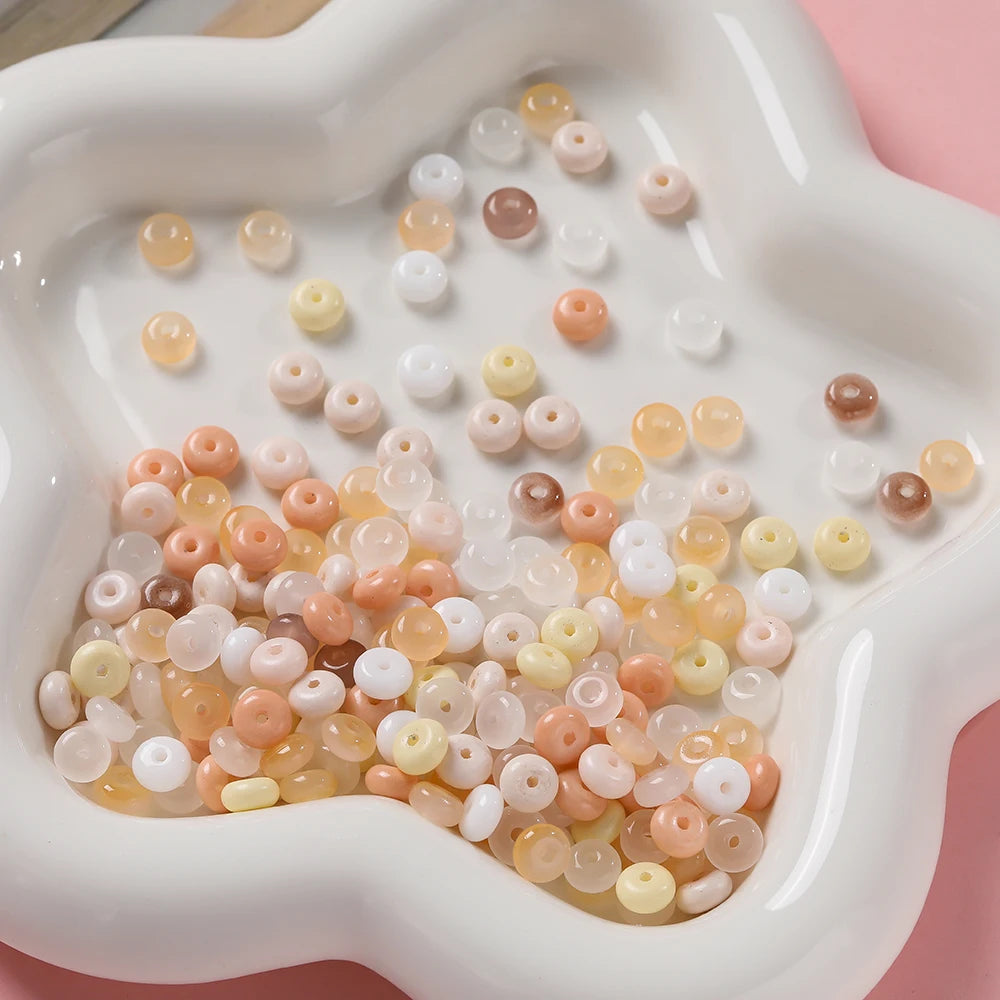 A close-up view of a white dish filled with various colored glass spacer beads including jade, pink, and clear shades.