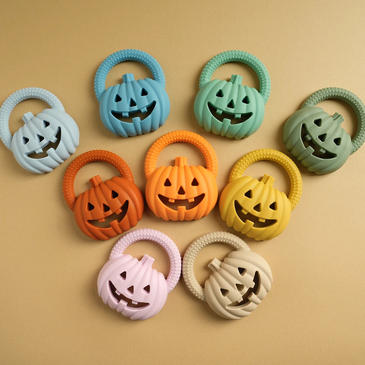 A collection of silicone pumpkin baby teethers in various colors including blue, green, orange, yellow, and pink.
