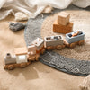 A wooden train toy carrying glass beads and labeled blocks on a textured beige surface.