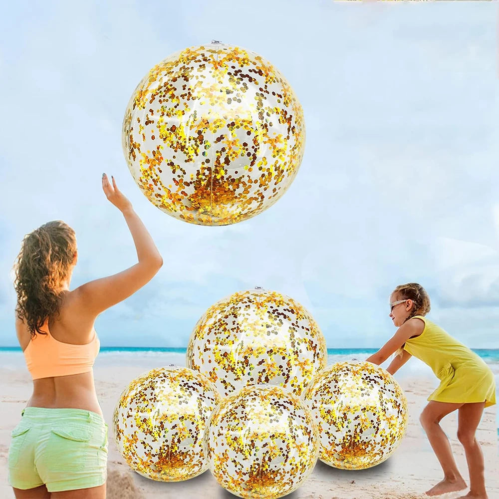 A woman is tossing a large, sequined inflatable beach ball high in the air against a bright blue sky and ocean backdrop.