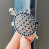 Silver rhinestone turtle brooch pin being held by a hand