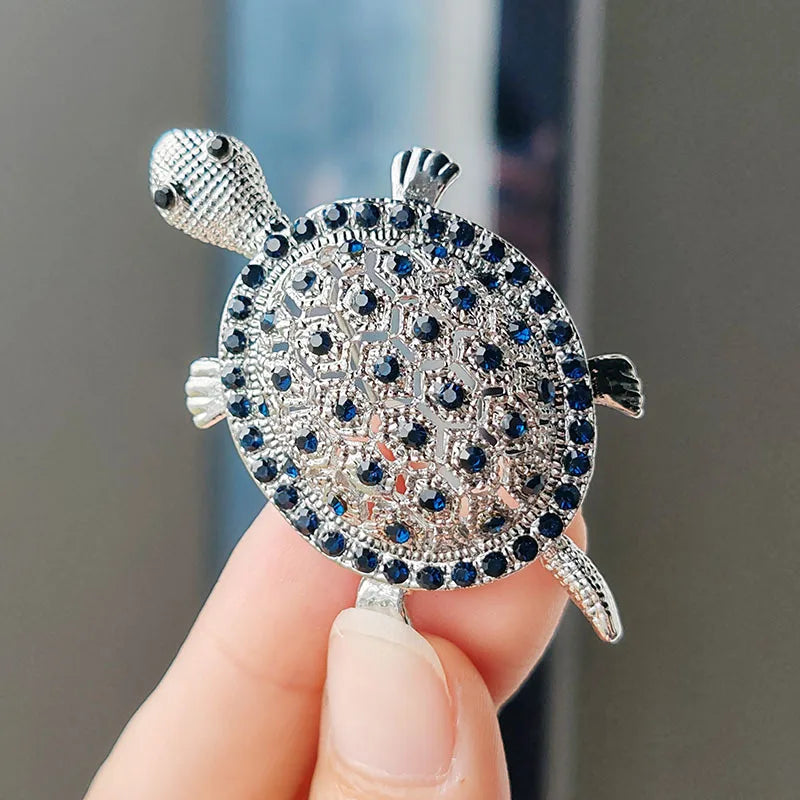 Silver rhinestone turtle brooch pin being held by a hand