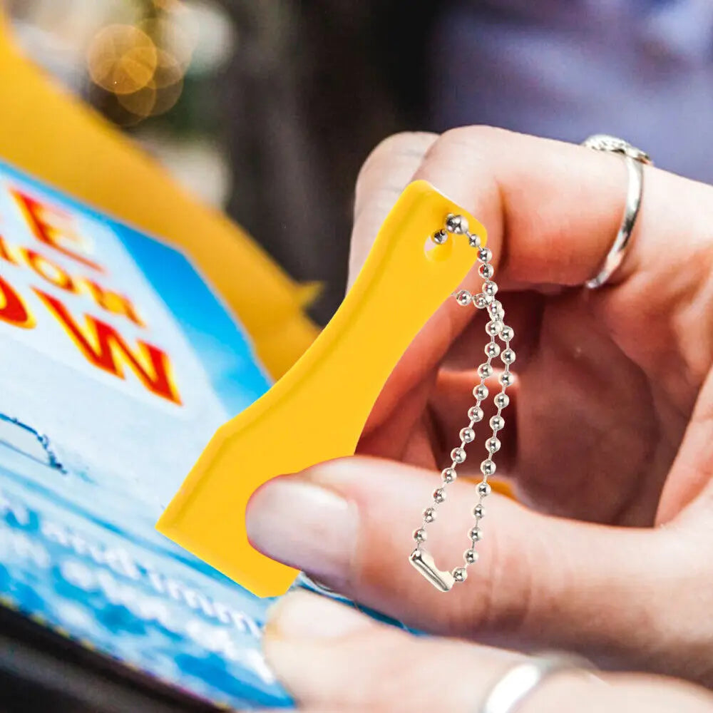 A hand holds a yellow plastic lottery scratcher keychain with a silver chain and a ring.