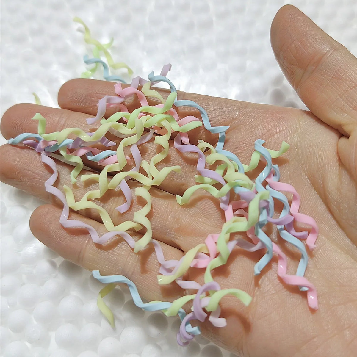 A hand holds a collection of colorful polymer clay marshmallow charms in various pastel shades.