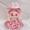 A plush doll wearing a pink strawberry patterned outfit with a bow and princess shoes, resting on white fur.