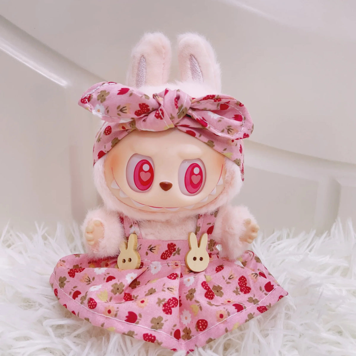 A plush doll wearing a pink strawberry patterned outfit with a bow and princess shoes, resting on white fur.