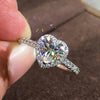 A close-up shot of a heart-shaped cubic zirconia ring being held by a finger, with sparkling light catching the stones.