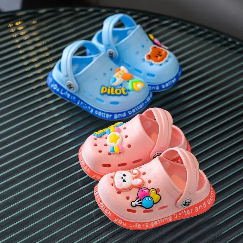 A pair of light blue and pink children's clogs for summer fun resting on a dark surface.