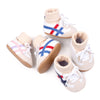 A pair of white baby booties with blue and red stripes and tan soles.