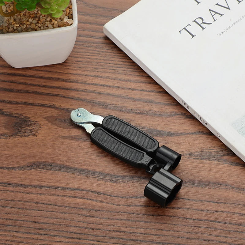 A black multi-tool for guitar strings, featuring a cutter and pin puller function, resting on a wooden surface.