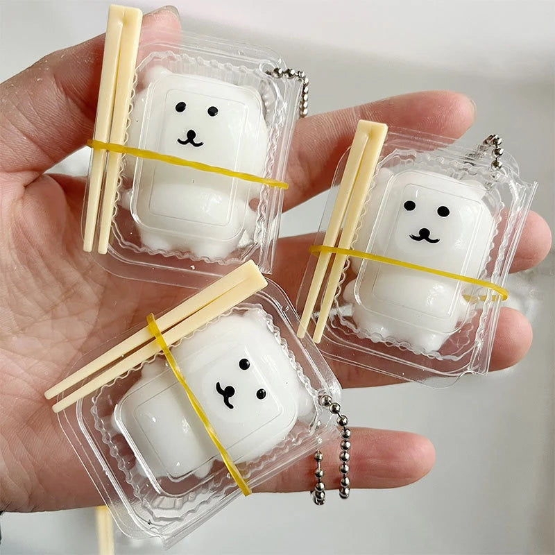 A hand holds three clear plastic pouches containing white squishy toys shaped like smiling white bears or dogs.