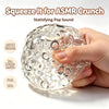 A hand squeezes a clear, spherical stress relief ball filled with ice beads for an ASMR crunch sound.