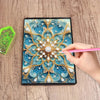 A hand is painting a detailed diamond art design featuring blue and gold floral patterns on a notebook.