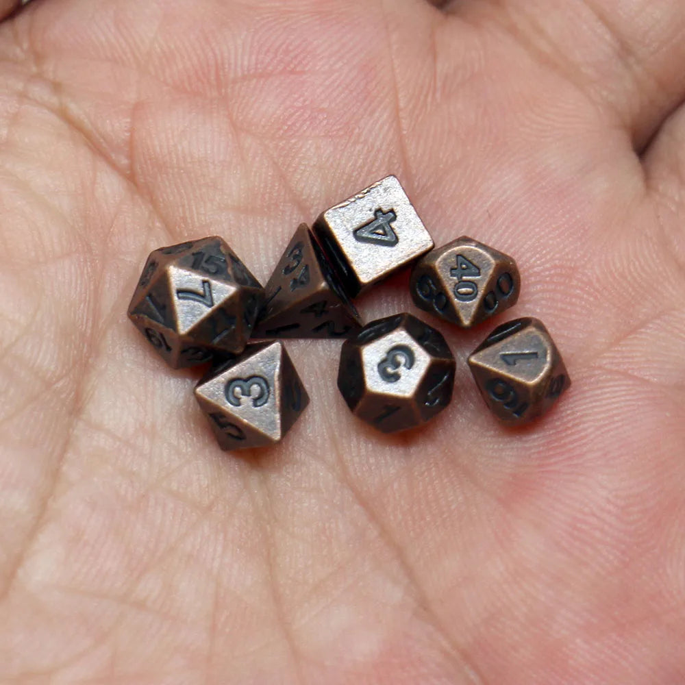 A set of seven antique metal polyhedral dice resting on a person's hand.