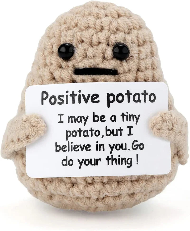 A handmade crochet plush toy resembling a potato with a positive message written on a white tag.