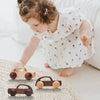 A young girl plays with a set of wooden Montessori push cart toys, including a car and a bus.
