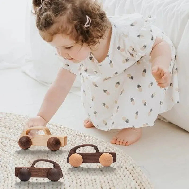 A young girl plays with a set of wooden Montessori push cart toys, including a car and a bus.