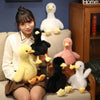 A young woman is sitting on a couch surrounded by various realistic call duck plush toys in white, black, and yellow colors.