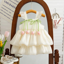 A white, sleeveless pleated princess dress for a baby girl with green ribbon details displayed in a wooden mirror frame.