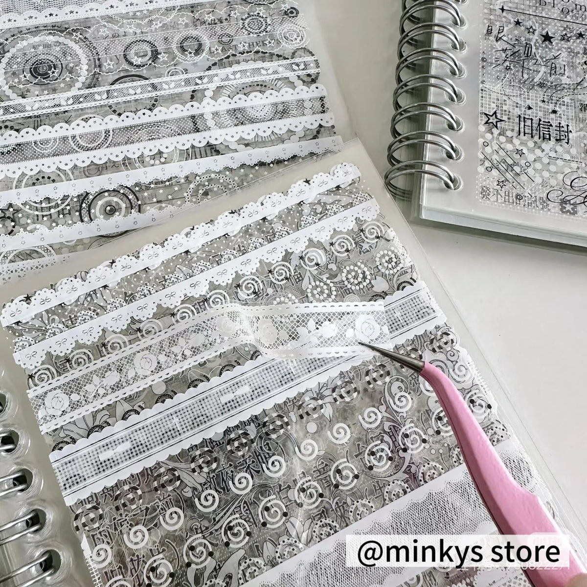 A close-up of a sheet of gray and white lace patterned sticker paper being cut with a precision craft knife.