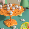 An orange plastic tree game with small white frog figures, showing a hand placing a frog onto the tree.