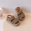 A pair of beige suede toddler sandals for boys and girls resting next to a white cup.