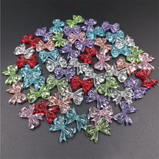 A scattered collection of 20 colorful acrylic bow beads in various shades of pink, purple, blue, and green.