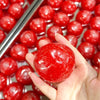 A hand holds a bright red watermelon ice sand squeeze toy with a crunchy sound, surrounded by other red spheres.
