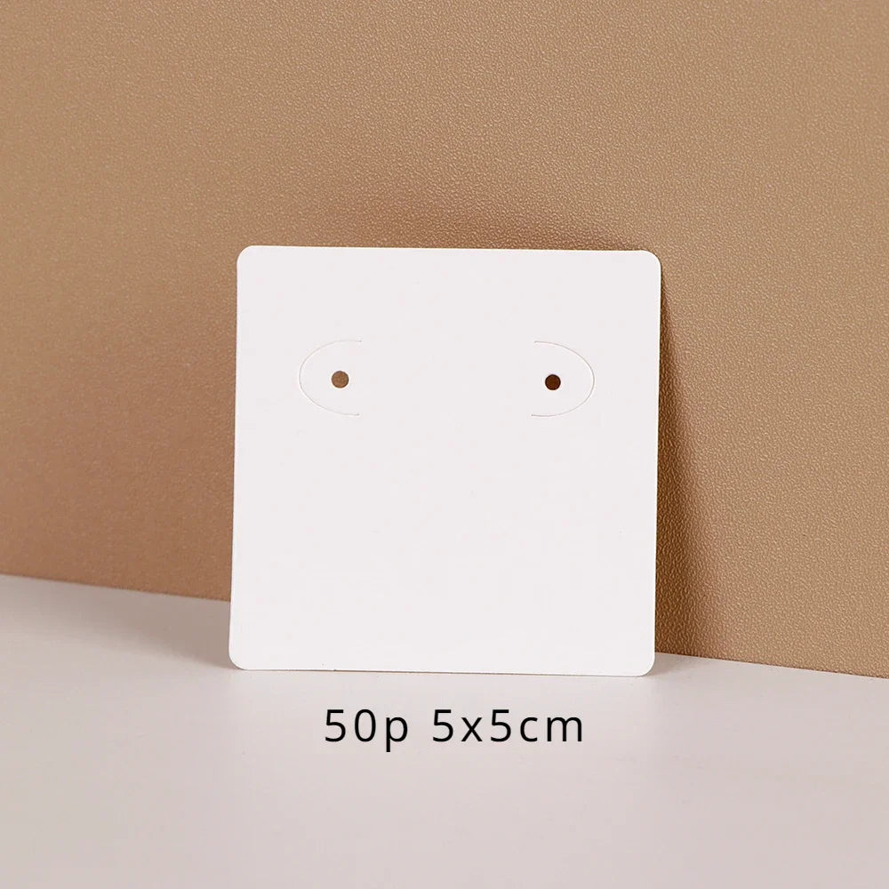 A white square jewelry display card with two small circular cutouts is shown against a beige background.