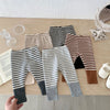 A flat lay of striped baby leggings in beige, black, and gray, showing various patterns and fabric textures.