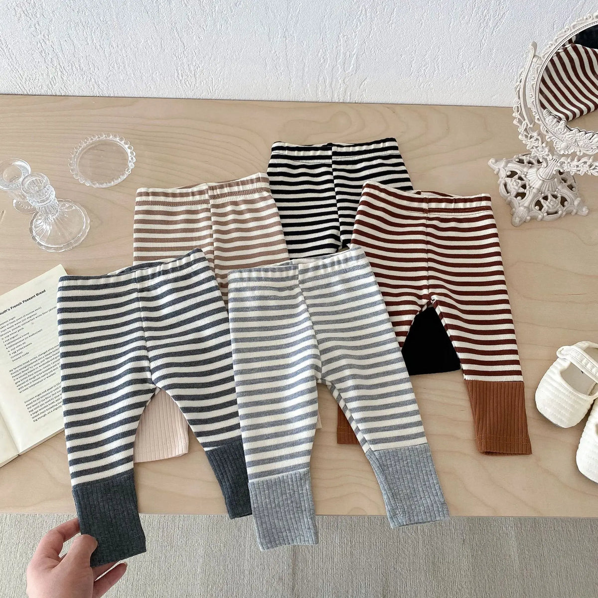 A flat lay of striped baby leggings in beige, black, and gray, showing various patterns and fabric textures.